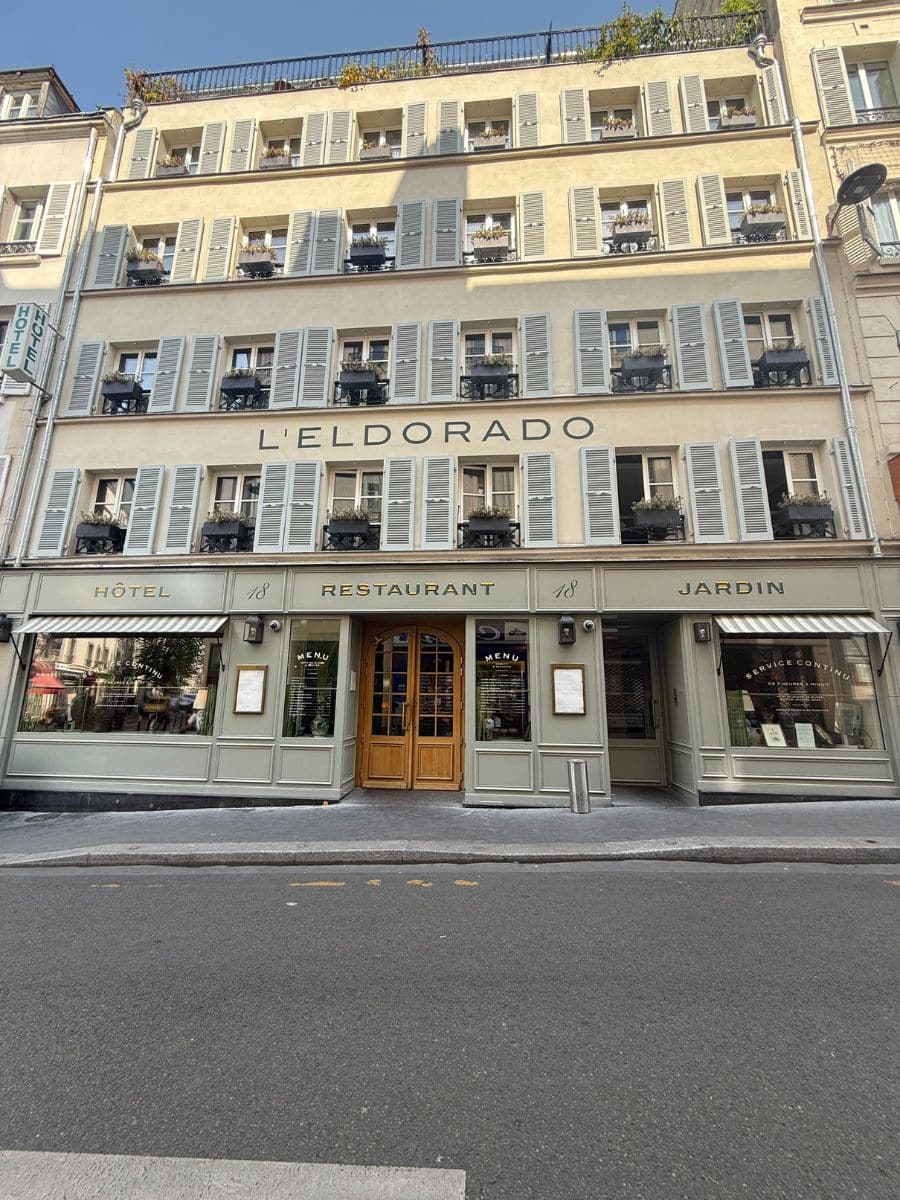Street-level view of Hotel Eldorado Paris with full facade showing symmetrical windows, signage, and a central wooden door entrance.