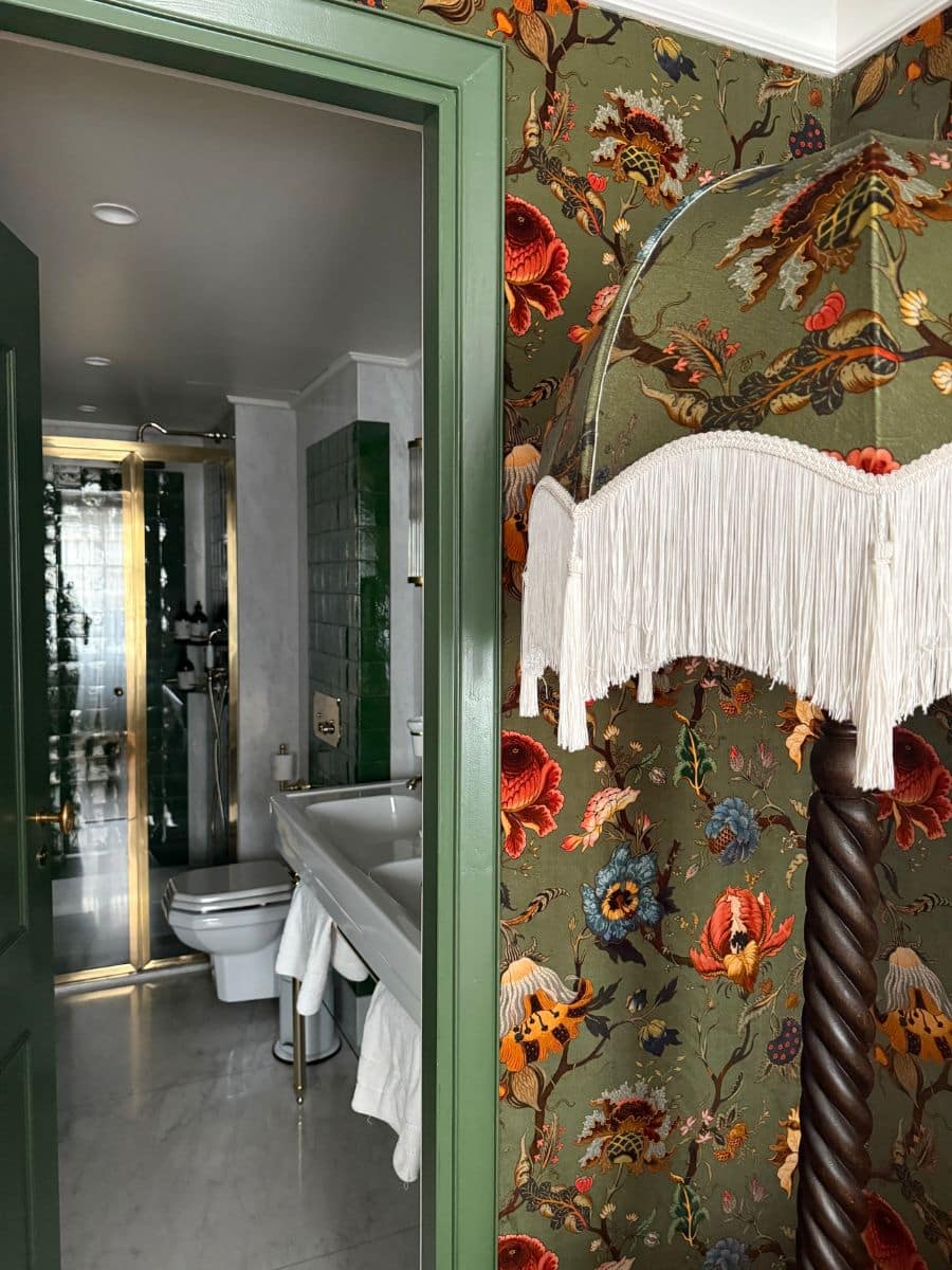 View from bedroom into the bathroom at Hotel Eldorado Paris, showing floral wallpaper, green doorframe, and white bathroom fixtures.