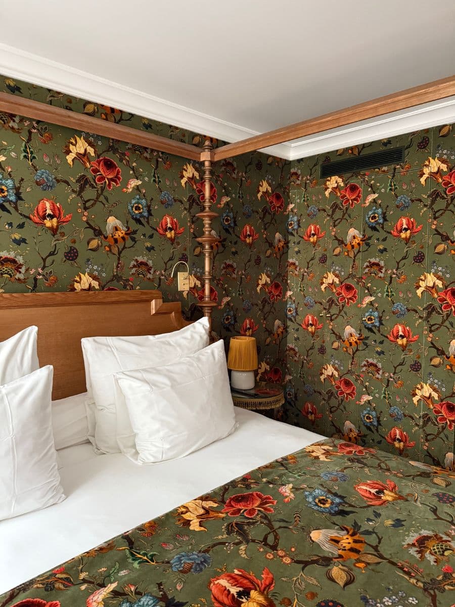 Canopy bed with crisp white pillows and floral-patterned bedding and wallpaper at Hotel Eldorado Paris.