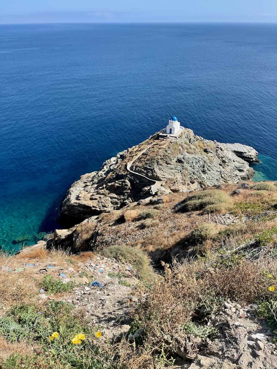Aerial view of a rocky promontory with a small white chapel overlooking the deep blue sea.