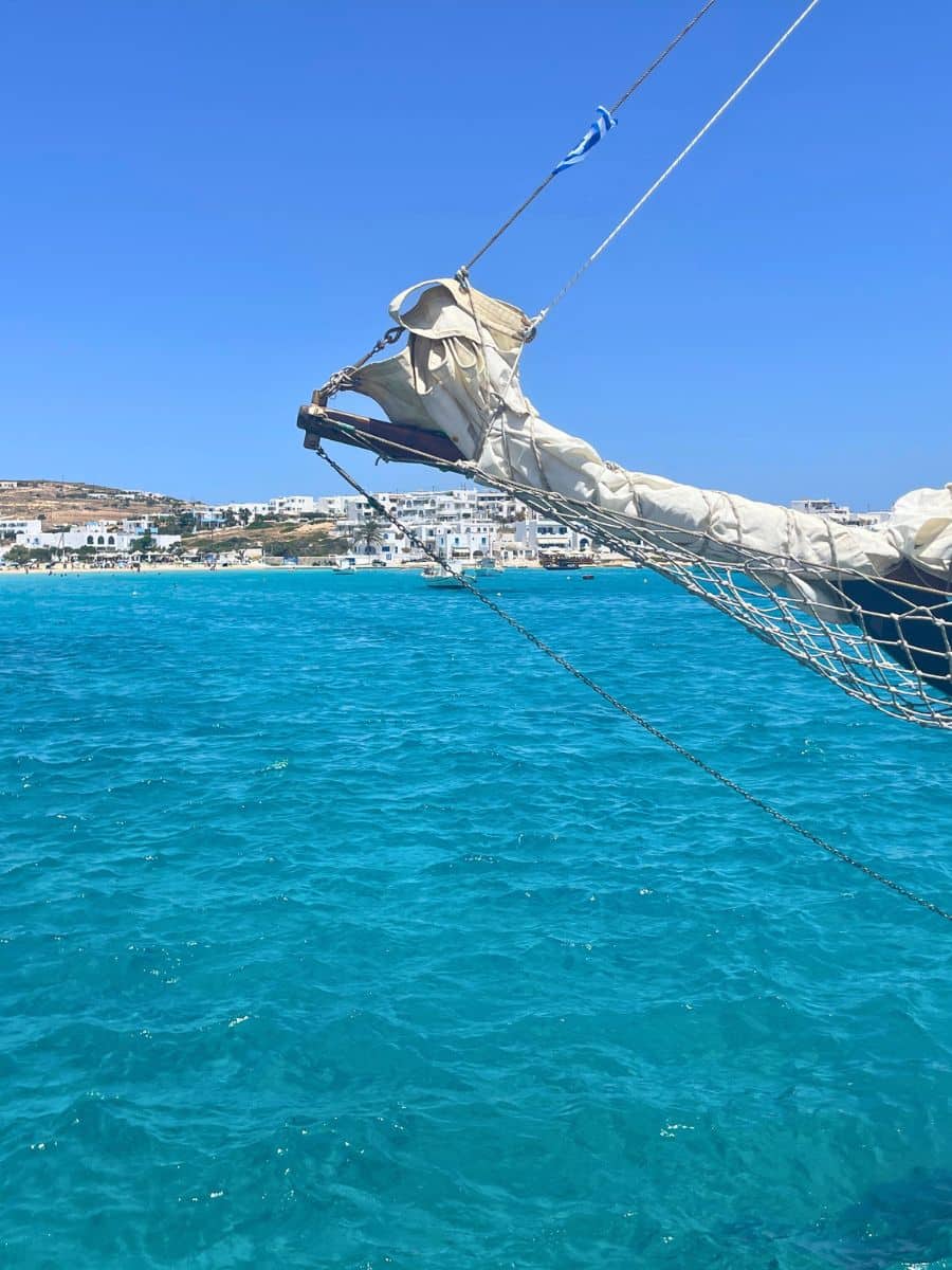 A traditional wooden sailing boat with ropes and rigging, floating on turquoise waters near a picturesque Greek island.