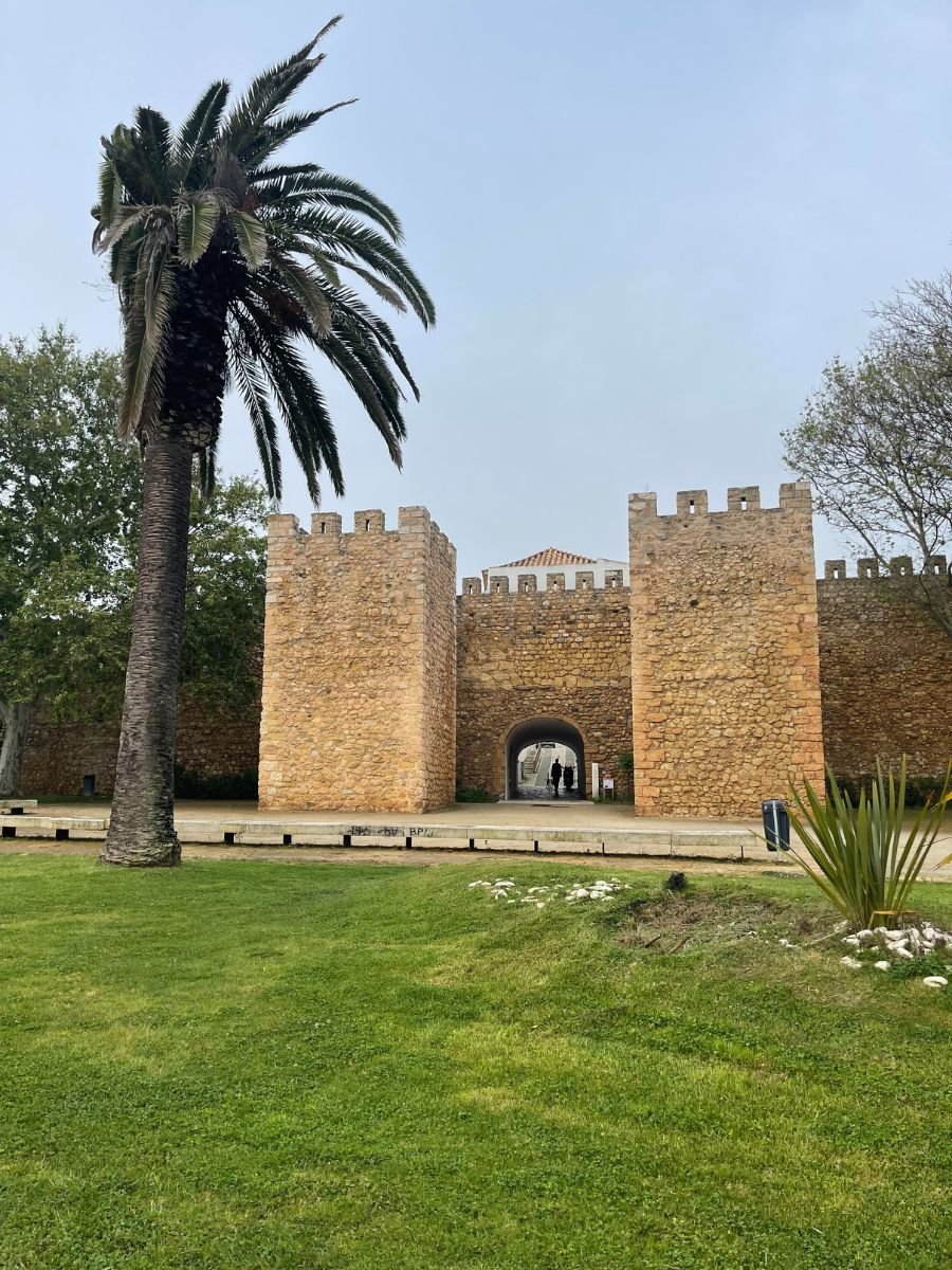 Stone gateway of the medieval city walls in Lagos, Portugal, with a palm tree and grassy courtyard