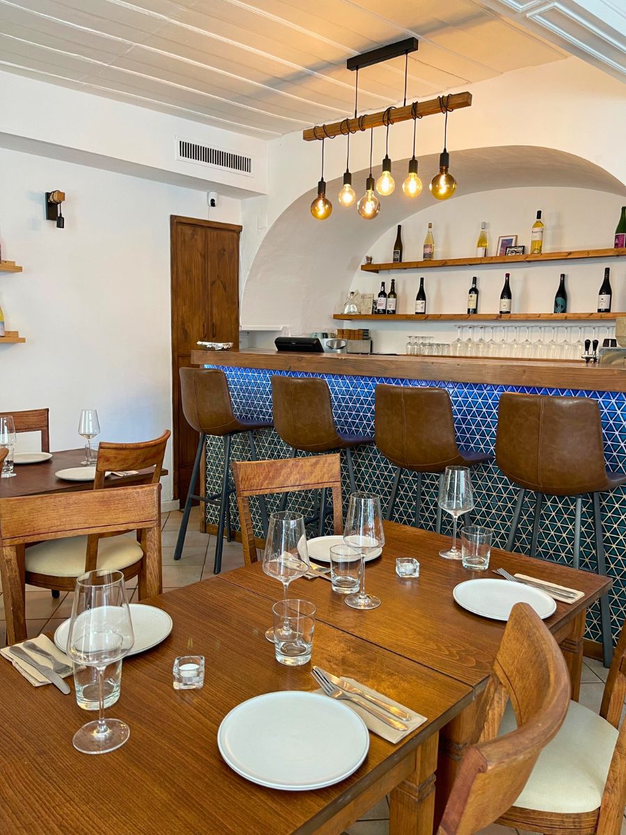 Interior of Travia restaurant in Lagos, featuring wooden tables, a blue-tiled bar, and warm modern lighting
