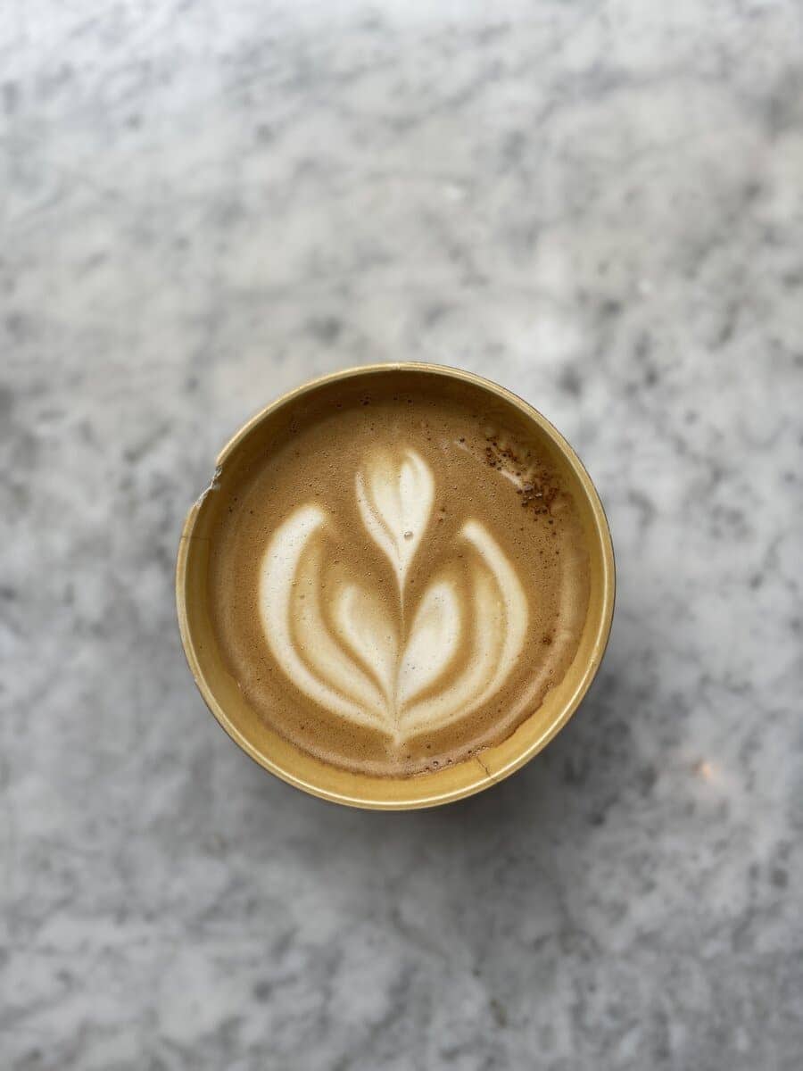 Artfully crafted latte at Atelier September, showcasing a detailed leaf design in the froth, served in a ceramic cup on a marble countertop.