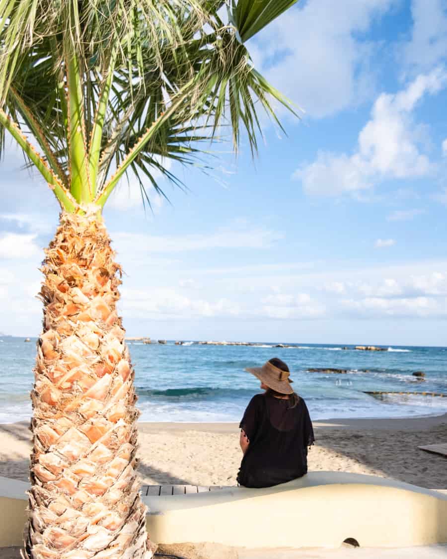 A woman at the beach in crete sitting under a palm tree