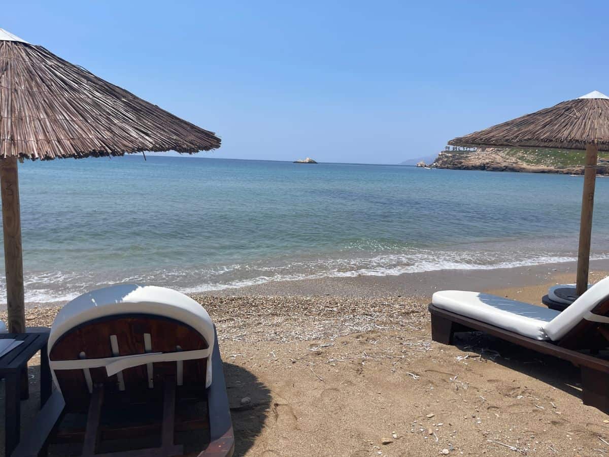 A beach with two empty beach chairs and umbrellas