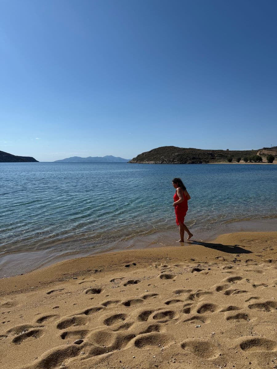 Woman in a red dress walking along a quiet sandy beach during a women-only Greece island tour