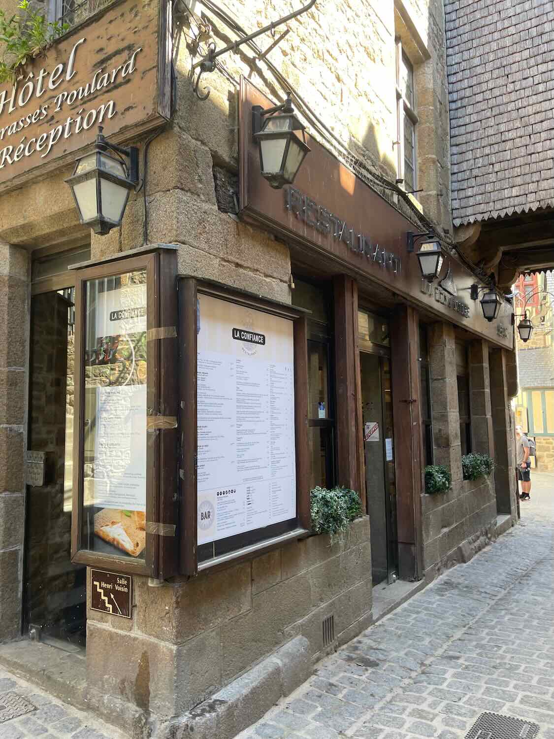 The facade of Hotel Terrasses Poulard in Mont Saint Michel, showcasing traditional architecture with a hanging sign and lanterns.