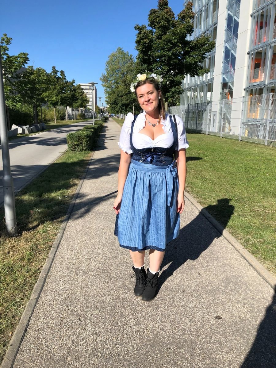 Woman in a traditional blue dirndl dress standing on a sunny pathway in Munich.