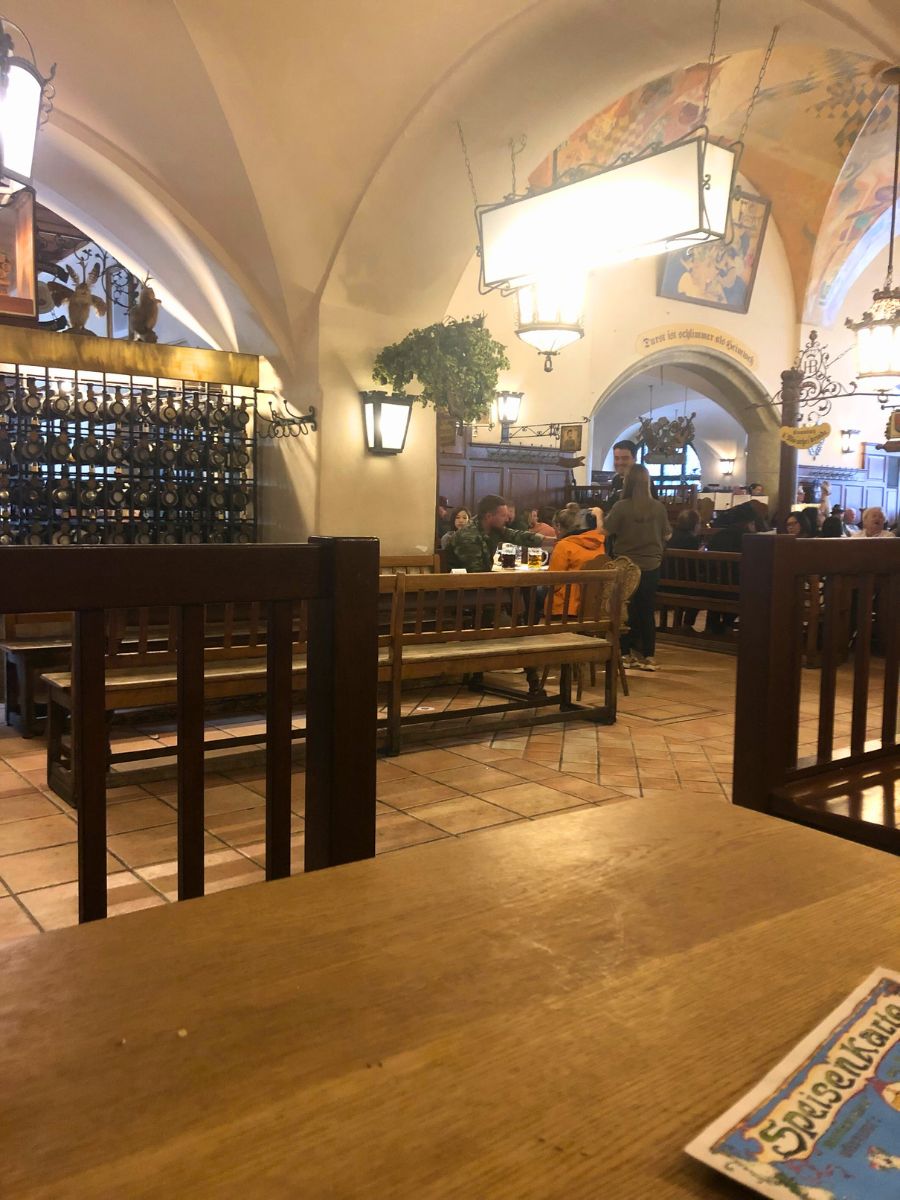 Interior of the Hofbräuhaus beer hall in Munich, showing wooden benches, arched ceilings, and diners enjoying their meals.