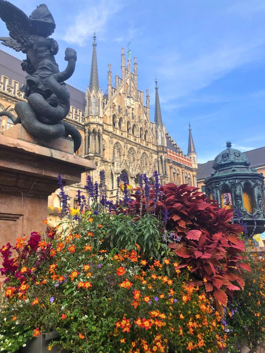 Colorful flowers and statue details in Marienplatz with the New Town Hall (Neues Rathaus) in Munich in the background.