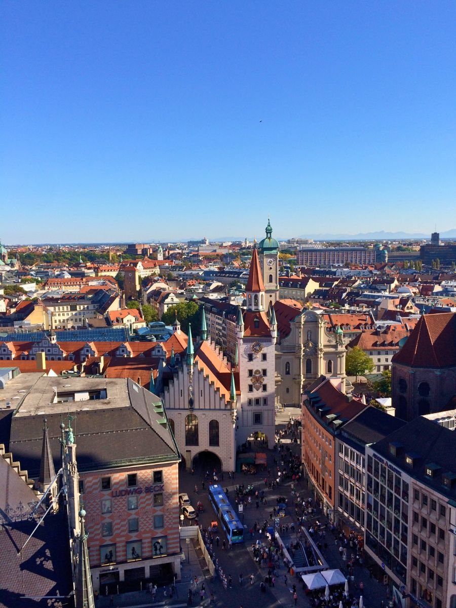 Aerial view of Munich’s Old Town showing Marienplatz, the Old Town Hall tower, and surrounding city rooftops under a clear blue sky.