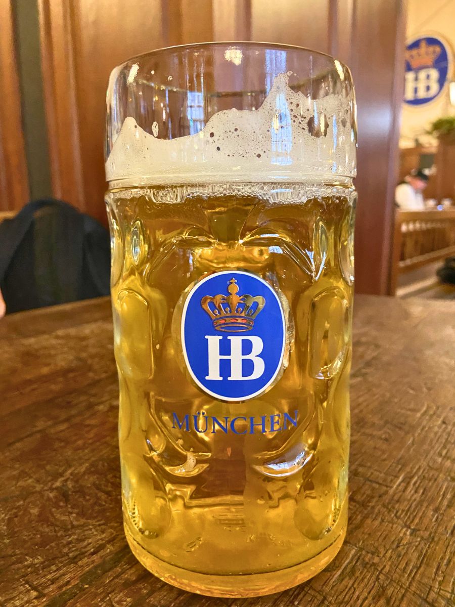 Large glass of beer served in a stein at the Hofbräuhaus in Munich, showing the blue HB logo.