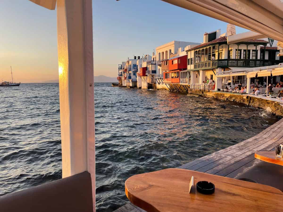 Sunset on the water in Mykonos with colorful houses and bars in the background