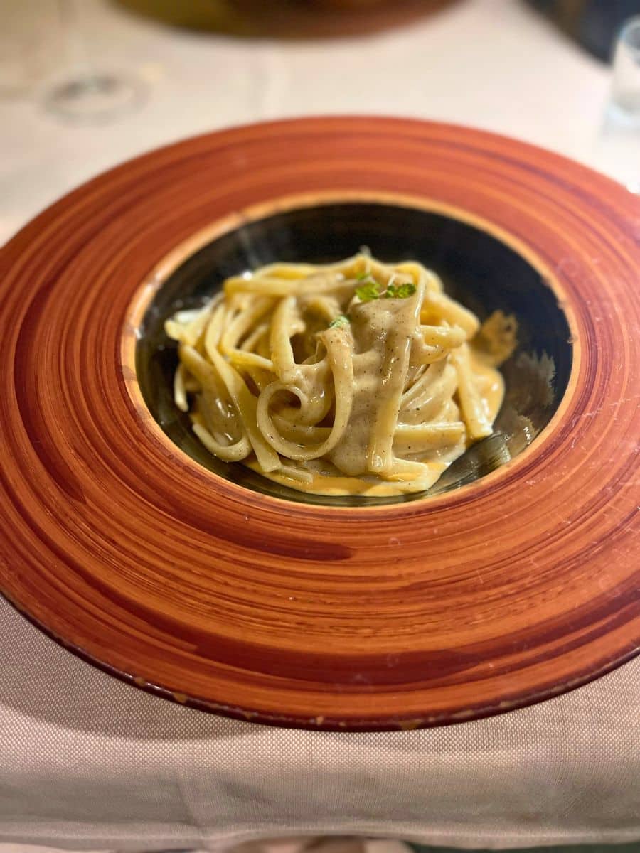 Plate of creamy pasta served in an elegant black and brown dish, garnished with herbs, creating a cozy and inviting presentation.