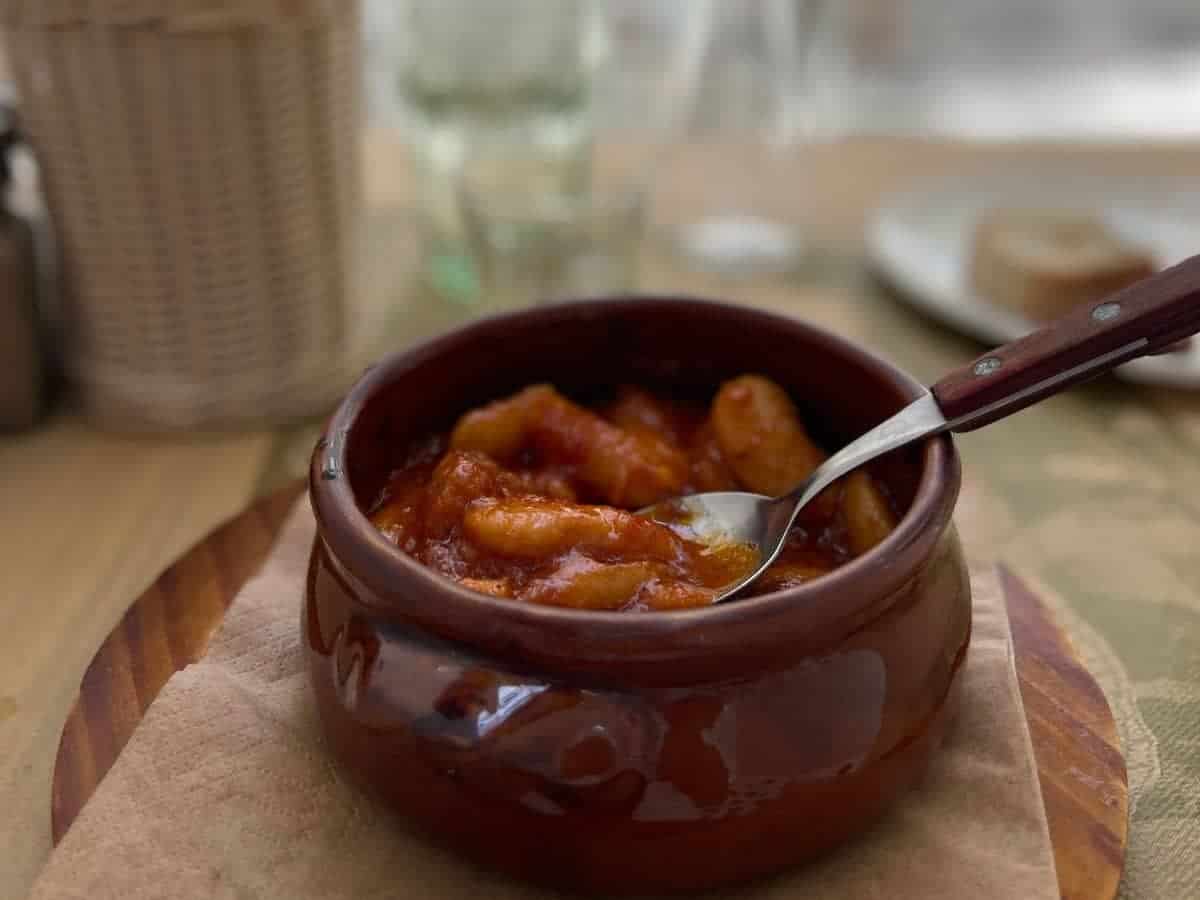 A bowl of giant beans in a red sauce. 