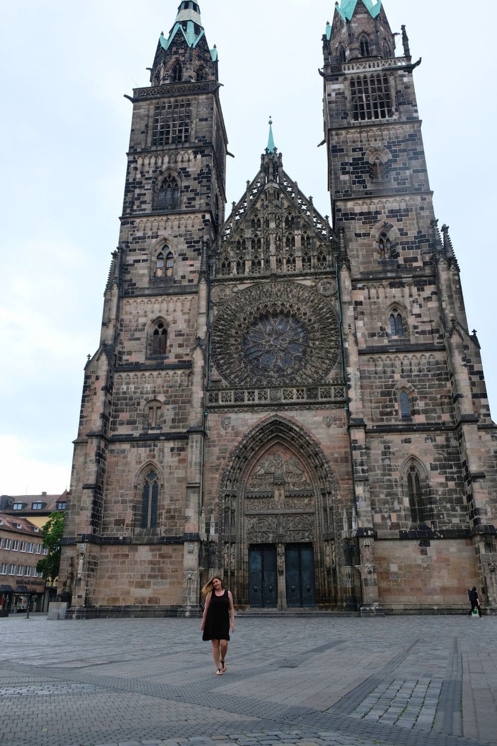 A woman standing in front of the majestic St. Lorenz Church in Nuremberg, an iconic stop on a day trip exploring the city's gothic landmarks