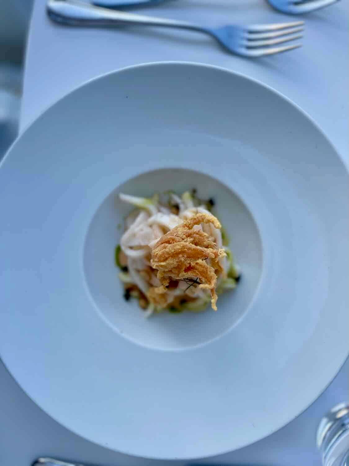 A gourmet dish beautifully presented on a white circular plate at Omilos restaurant, with a focus on the local cuisine of Hydra, Greece