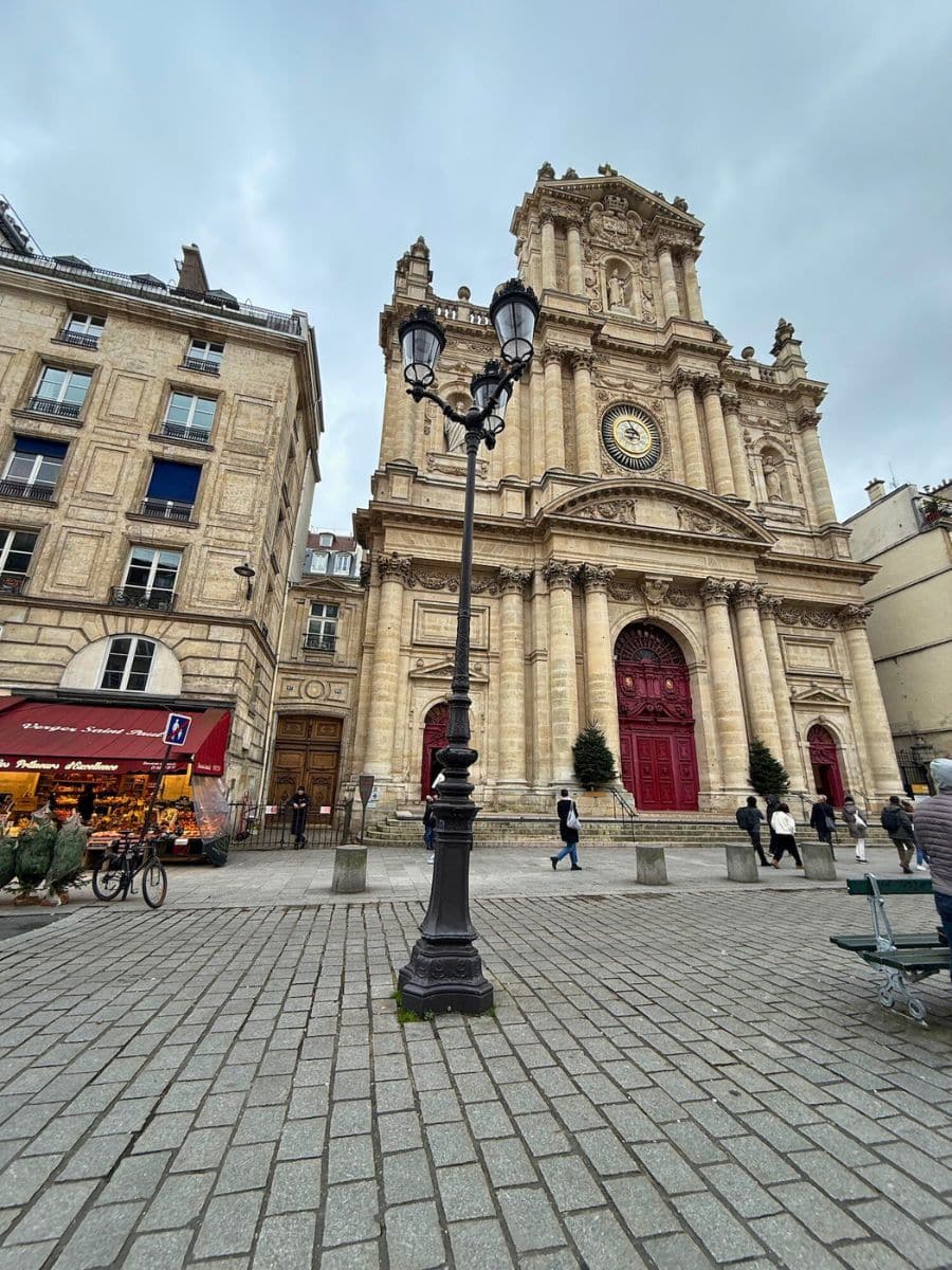 A grand church with a clock on its facade and red doors, surrounded by cobblestone streets and neighboring buildings.