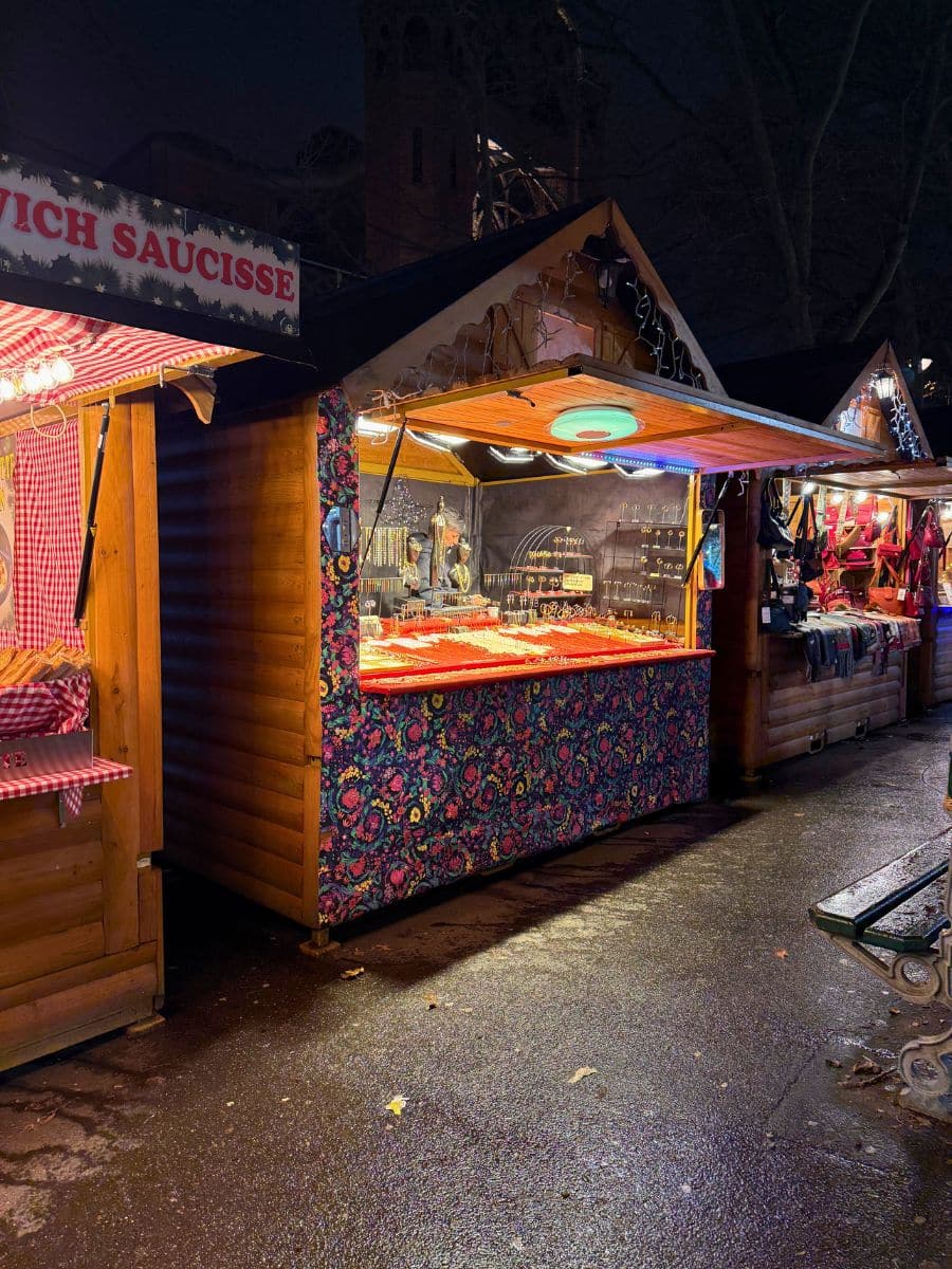 A festive wooden stall at a Paris Christmas market, brightly lit and adorned with colorful decorations, displaying various goods for sale.
