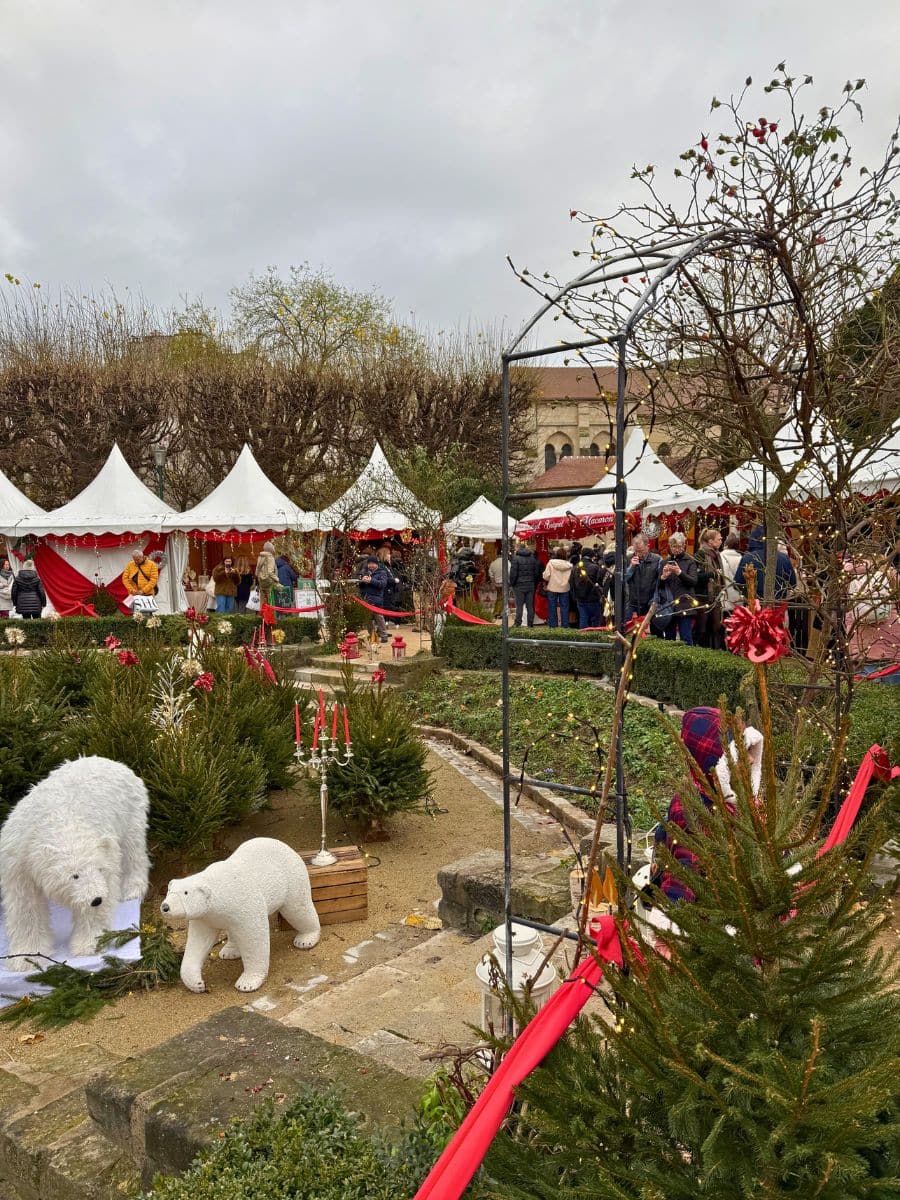 A festive Christmas market in Paris with white tents, decorated with red ribbons, and surrounded by greenery and polar bear statues.