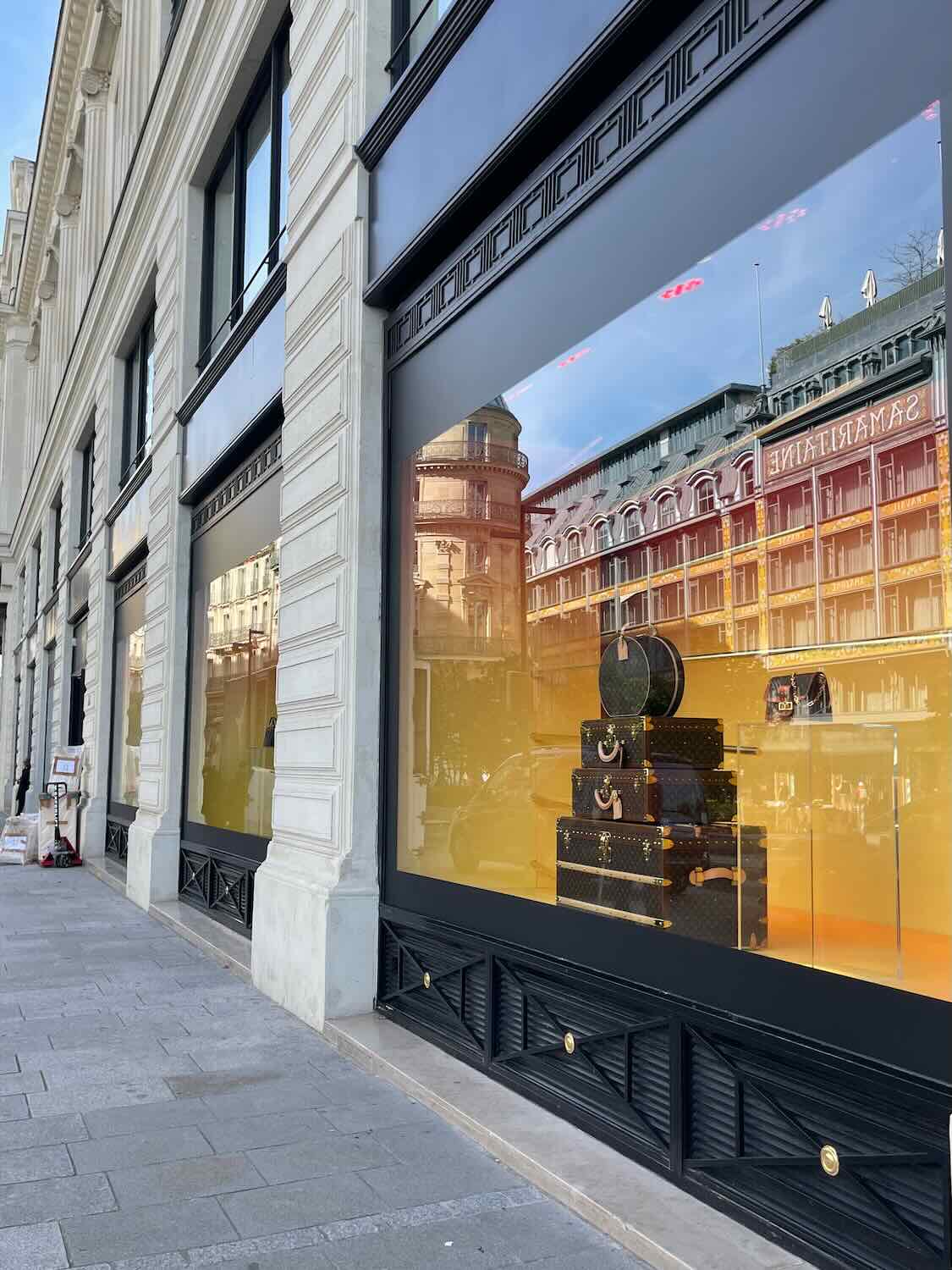 A reflective shop window displays luxury bags on a golden backdrop, with the architecture of Paris mirrored in the glass, symbolizing the city's chic and stylish atmosphere.