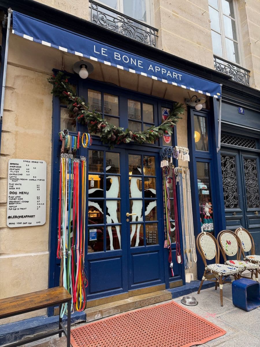 A dog-friendly café storefront in Paris named "Le Bone Appart," featuring colorful leashes, a festive garland, and a special dog menu displayed outside.