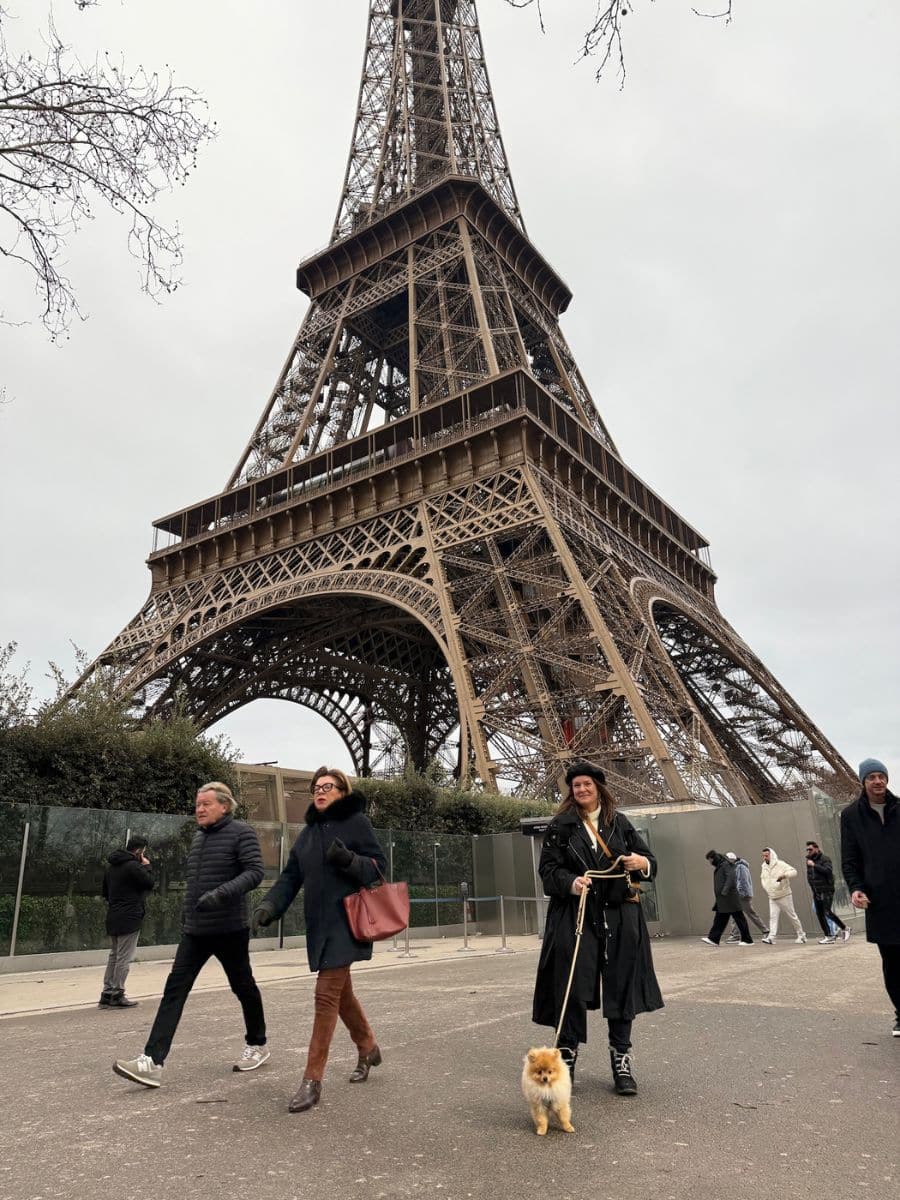Melissa and Teddy near the Eiffel Tower in Paris, with other pedestrians and an overcast sky in the background.