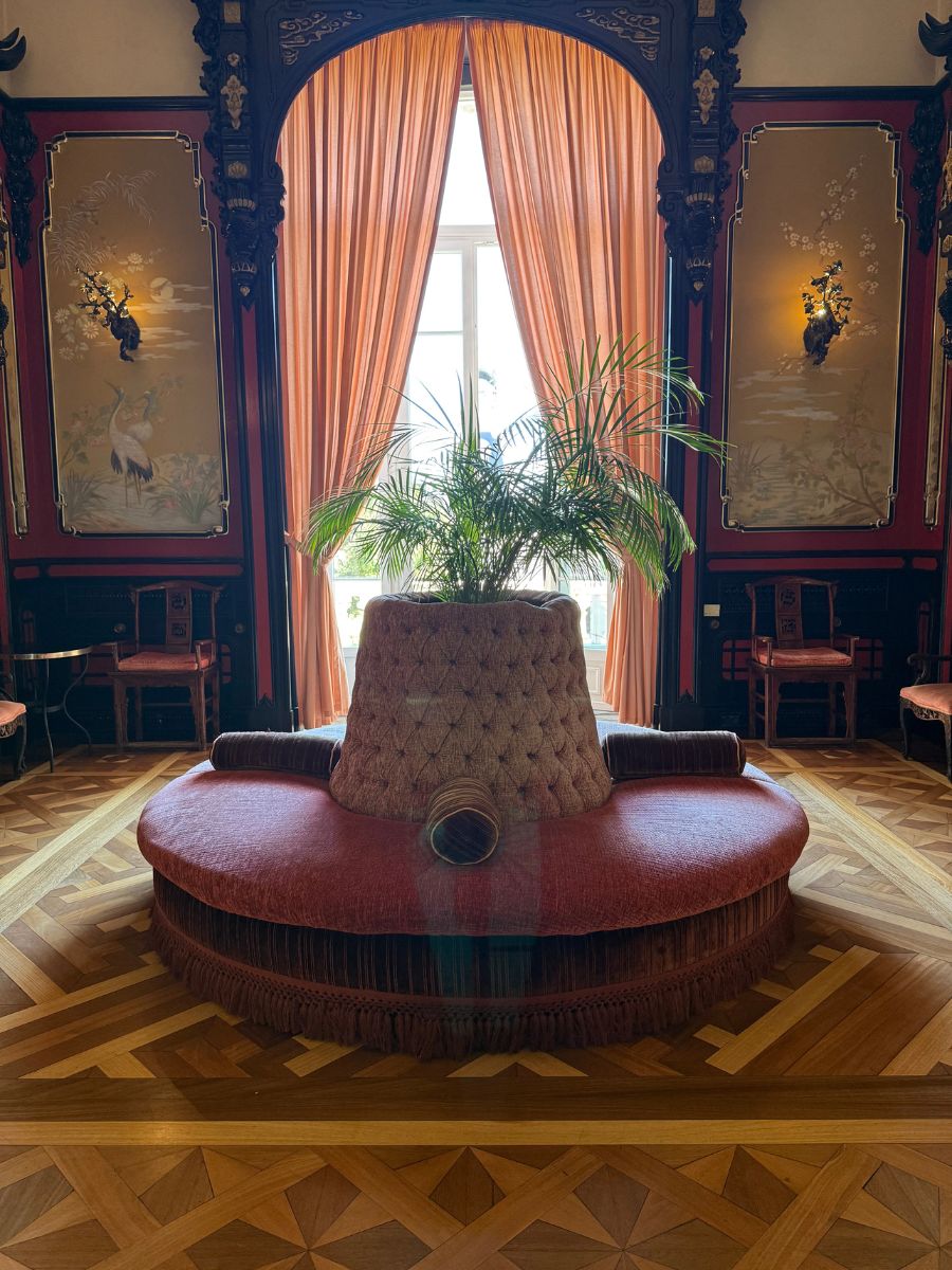 Luxurious lounge room at Pestana Palace Lisboa with ornate Asian-inspired wall panels, elegant peach drapes, and a circular tufted velvet seating area.