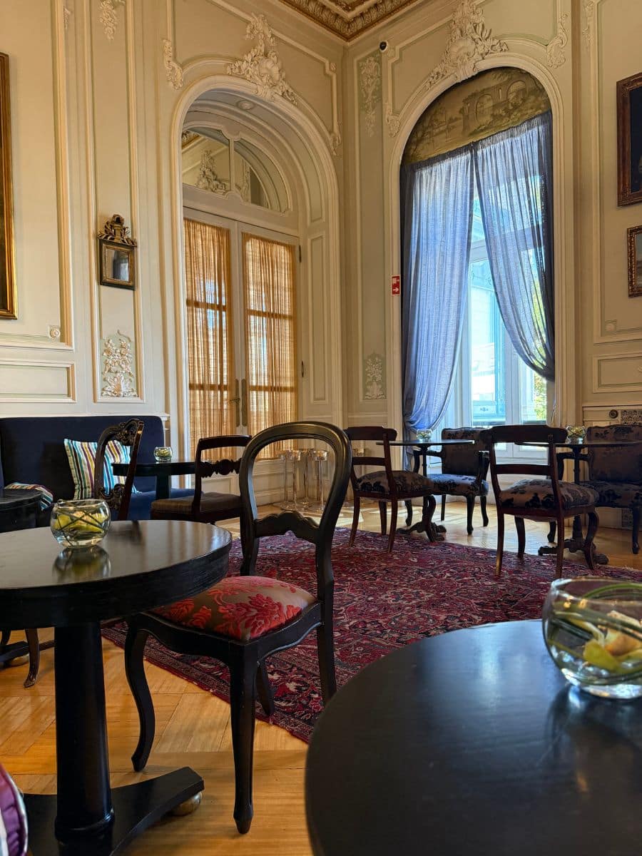 Refined lounge at Pestana Palace Lisboa with vintage chairs, ornate wall details, and natural light filtering through tall windows.