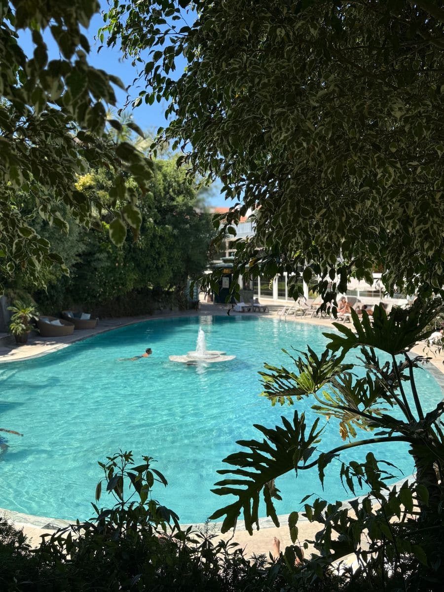 Tropical-style outdoor pool at Pestana Palace Lisboa, framed by lush greenery and featuring a central fountain.