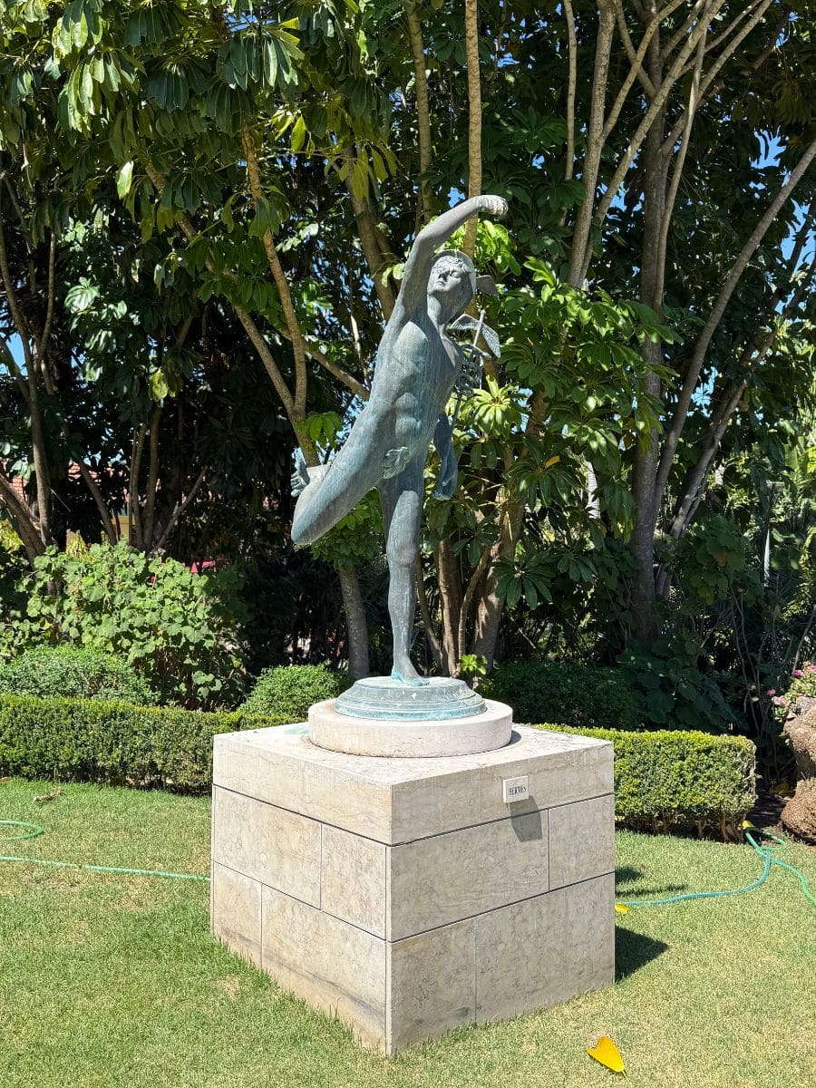 Bronze statue of Hermes displayed in the gardens of Pestana Palace Lisboa, surrounded by lush greenery.