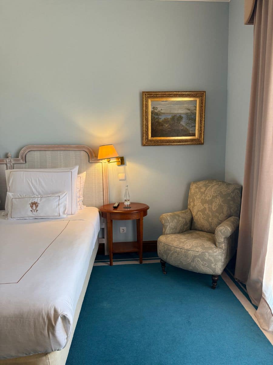 Cozy corner of a hotel room at Pestana Palace Lisboa with an upholstered armchair, side table, and framed landscape painting beside the bed.