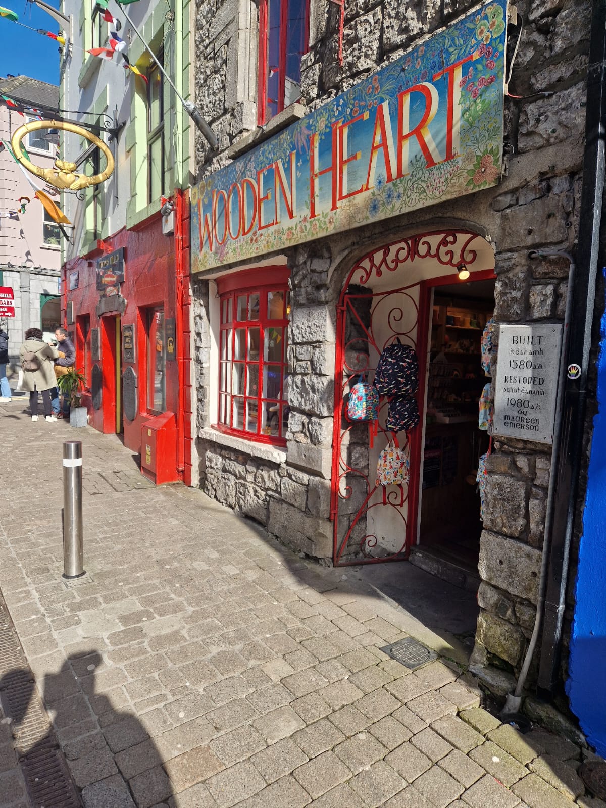 The entrance to "Wooden Heart," a charming shop housed in a historic stone building in Galway. The bright red windows and door, along with a decorative sign, create a cozy and inviting atmosphere.