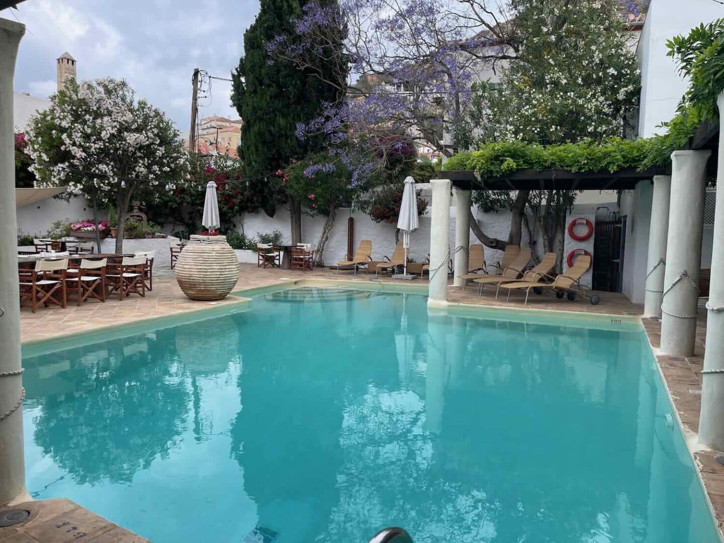 Luxurious swimming pool area in a Hydra hotel, fringed by white architecture, purple blooms, and an inviting lounge area, perfect for a day of relaxation