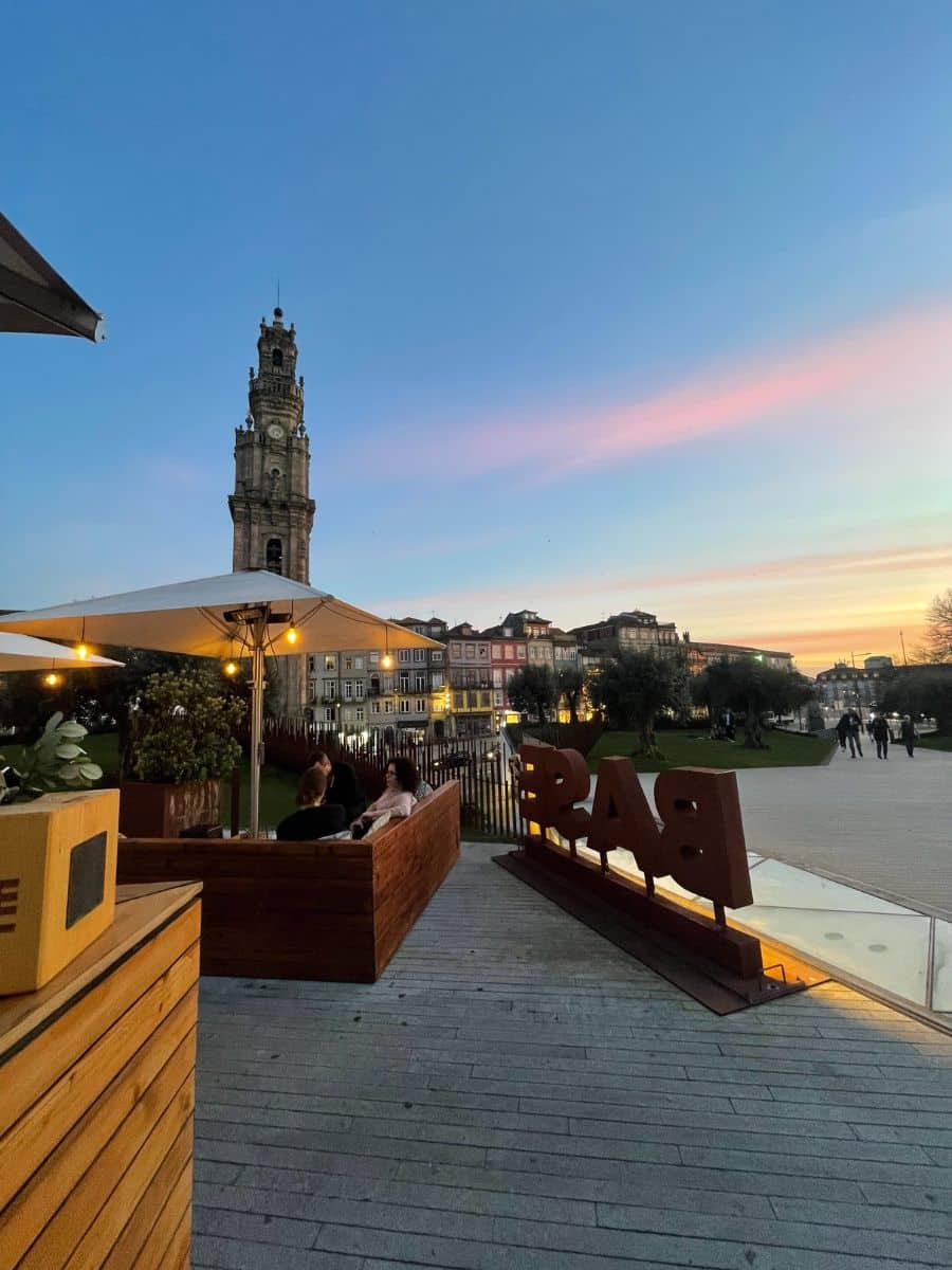 A sunset view from a rooftop bar in Porto, Portugal, with the Clérigos Tower standing tall against a pastel-colored sky.