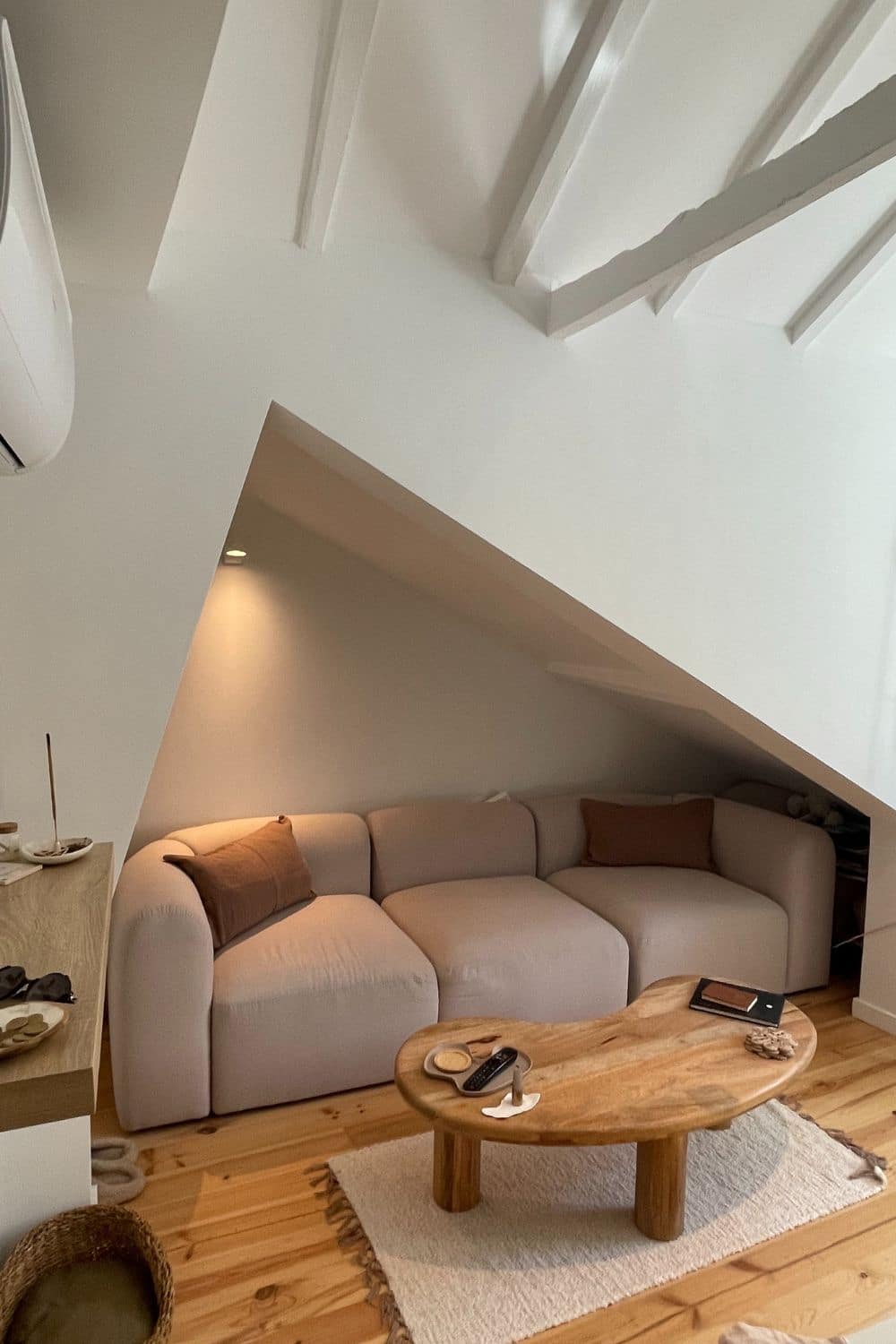 Cozy living area in an Airbnb with a plush cream sofa under a slanted ceiling, accented by natural wood elements and soft lighting, creating a warm and inviting space.