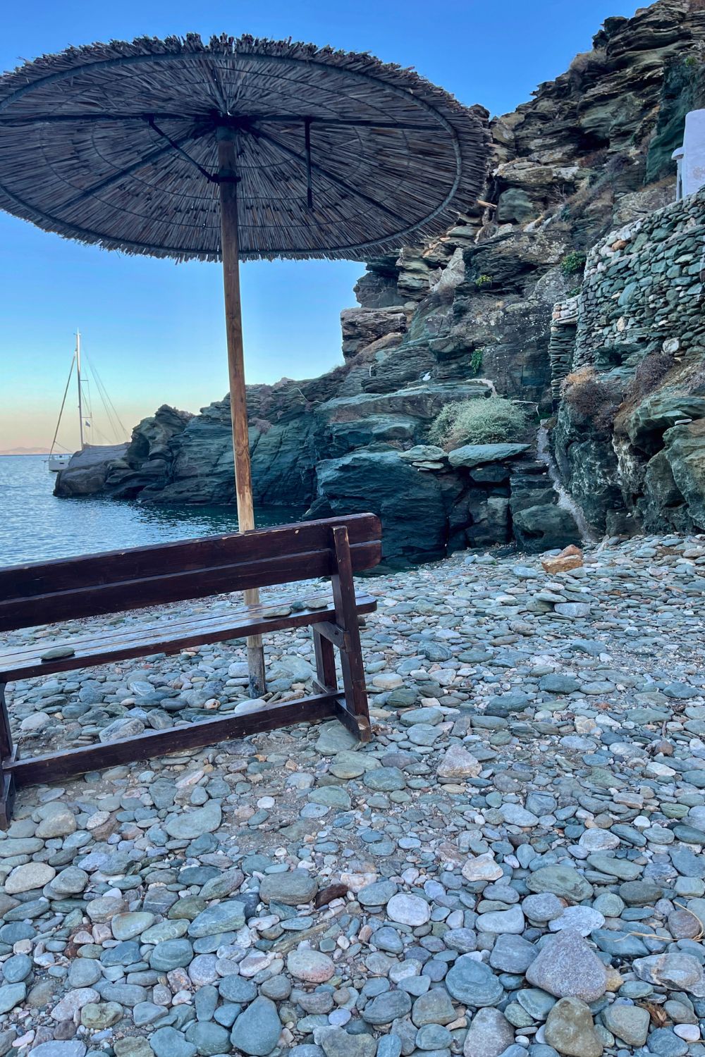 A single straw parasol stands above a rocky beach in Sifnos, inviting relaxation beside the serene Aegean waters.