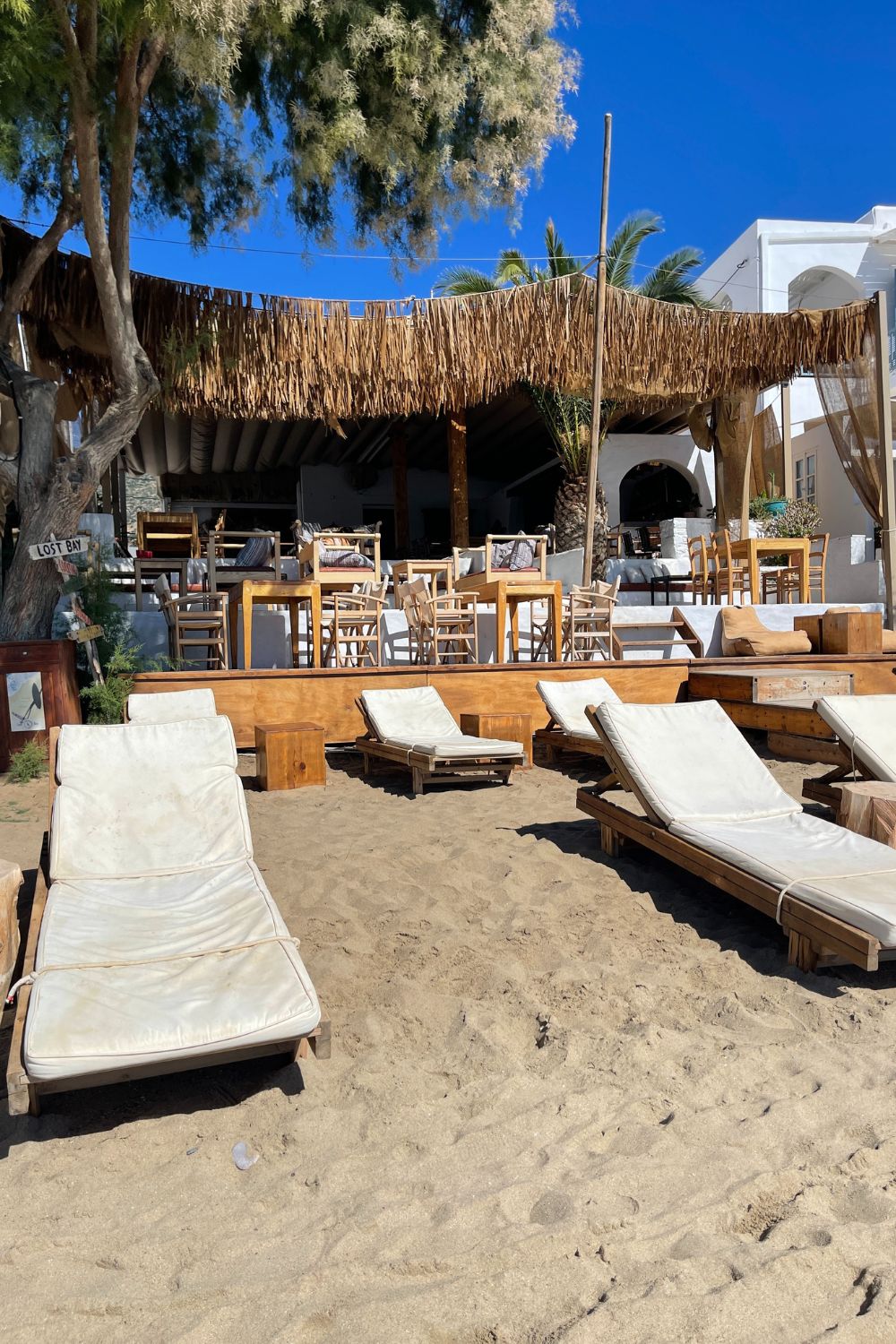 Luxurious beach loungers under natural straw umbrellas on a sandy Sifnos beachfront, offering a perfect spot for seaside leisure.