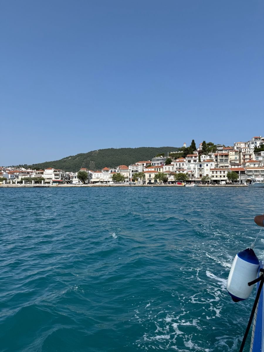 View of Skiathos Town’s white buildings and red rooftops from the water, with a boat's edge and a fender in the foreground under a clear blue sky.