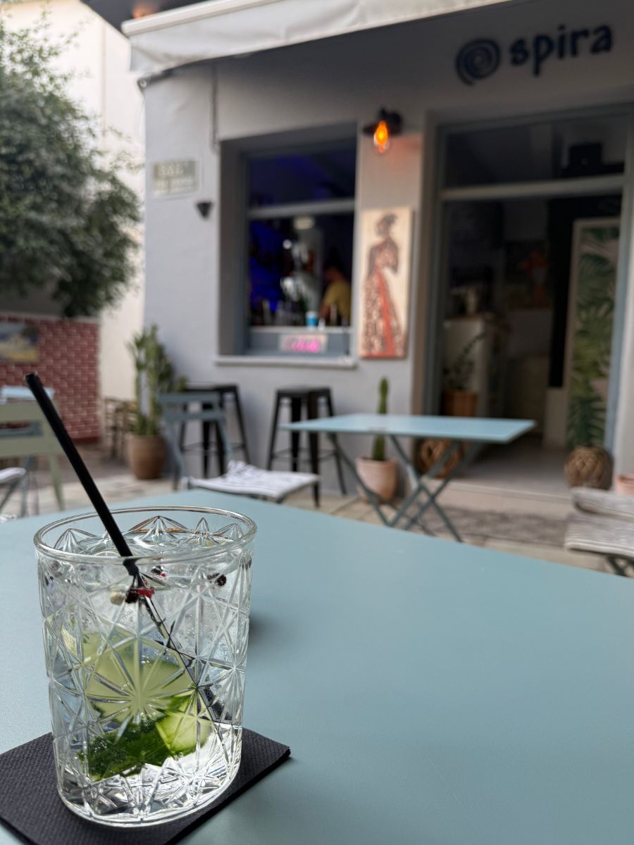 A refreshing cocktail with cucumber and herbs in a crystal glass on a teal table, in front of Spira bar in Skiathos, Greece.