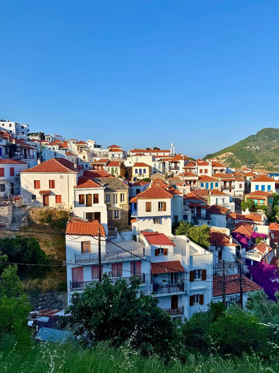 Scenic hillside view of Skopelos town with traditional whitewashed houses and terracotta roofs under a clear blue sky.