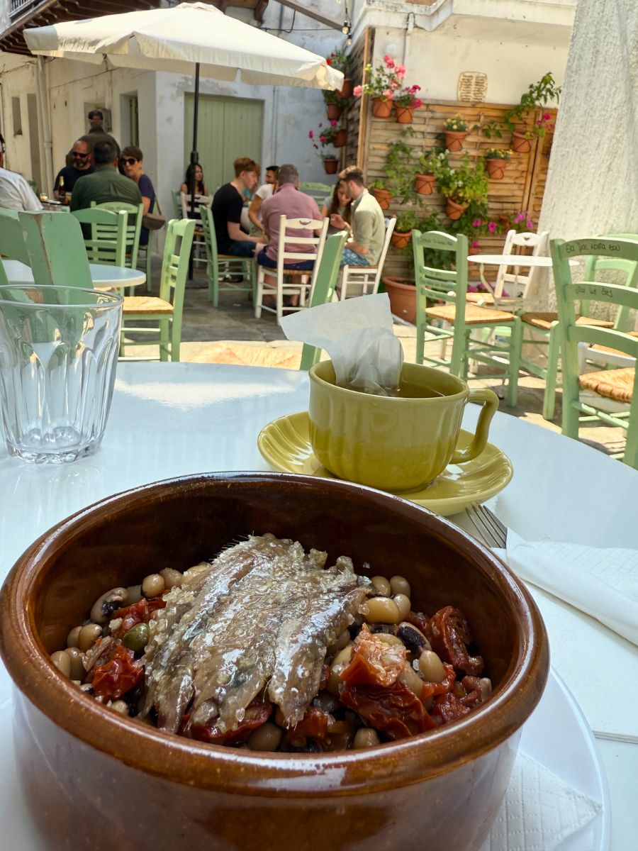 Traditional Greek bean salad with sardines served in a clay bowl at an outdoor courtyard café in Skopelos.