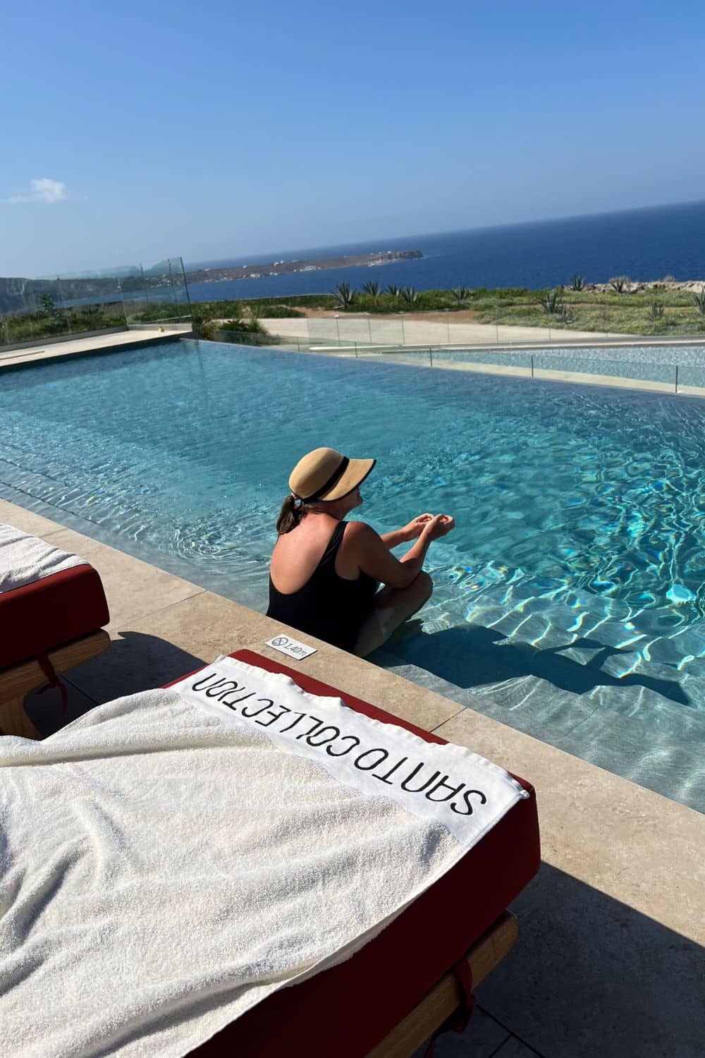 A woman relaxing by an infinity pool overlooking a stunning coastal view, reflecting a serene and luxurious holiday setting.