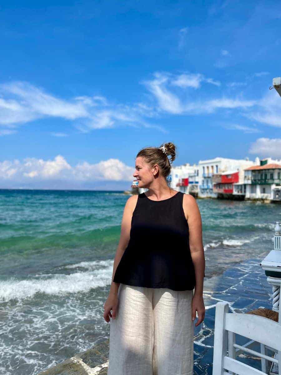 a solo woman traveling in her 40's in Mykonos with the ocean and restaurants in the background