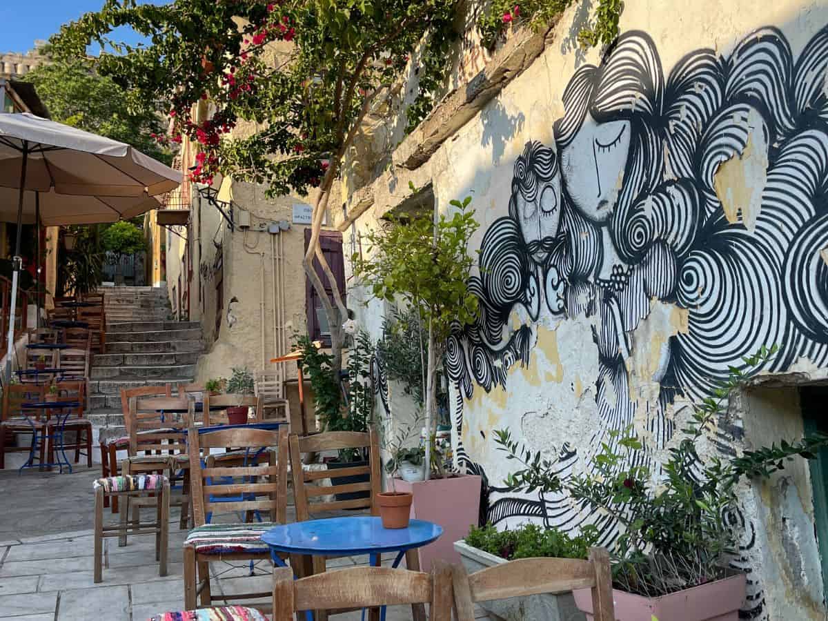 Tables and chairs with Athens street art on the wall.
