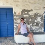 A woman sitting a bench next to a blue door in Greece.