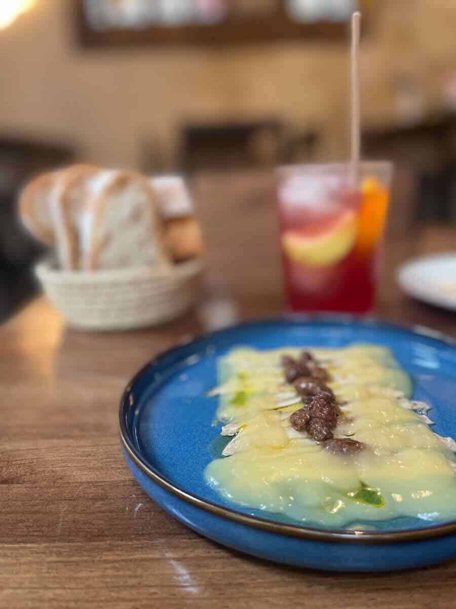 A close-up of a tapas plate with thinly sliced fish drizzled in sauce, paired with a refreshing red drink garnished with fruit, creating a delightful and inviting dining scene in Valencia.