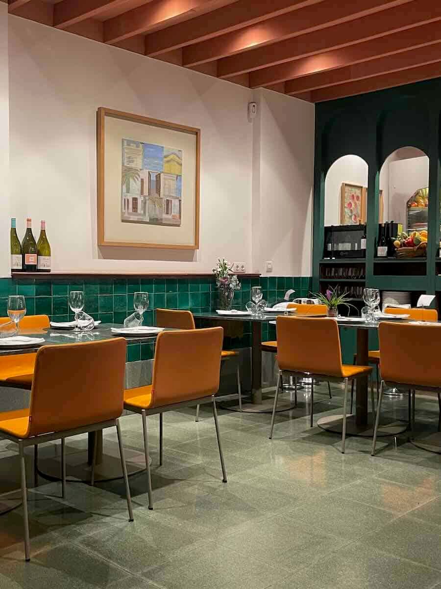 Cozy interior of a Valencia restaurant, featuring green tile, warm lighting, and vibrant orange chairs, offering an inviting atmosphere for the experienced solo diners exploring local cuisine.