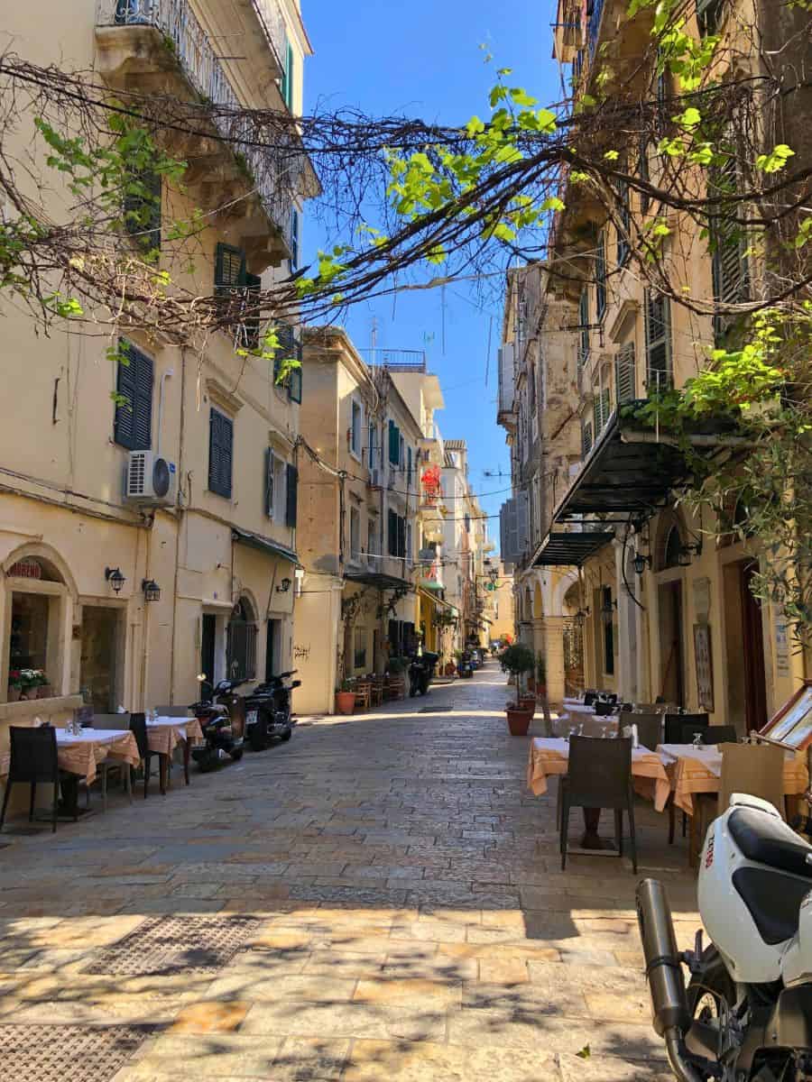 A small street in Corfu with vines between the buildings.